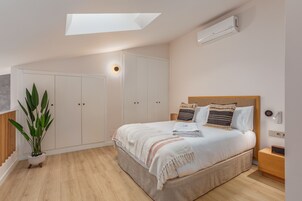 Un dormitorio con tragaluz, una cama con almohadas, una mesita de noche y un armario, además de una planta en maceta.