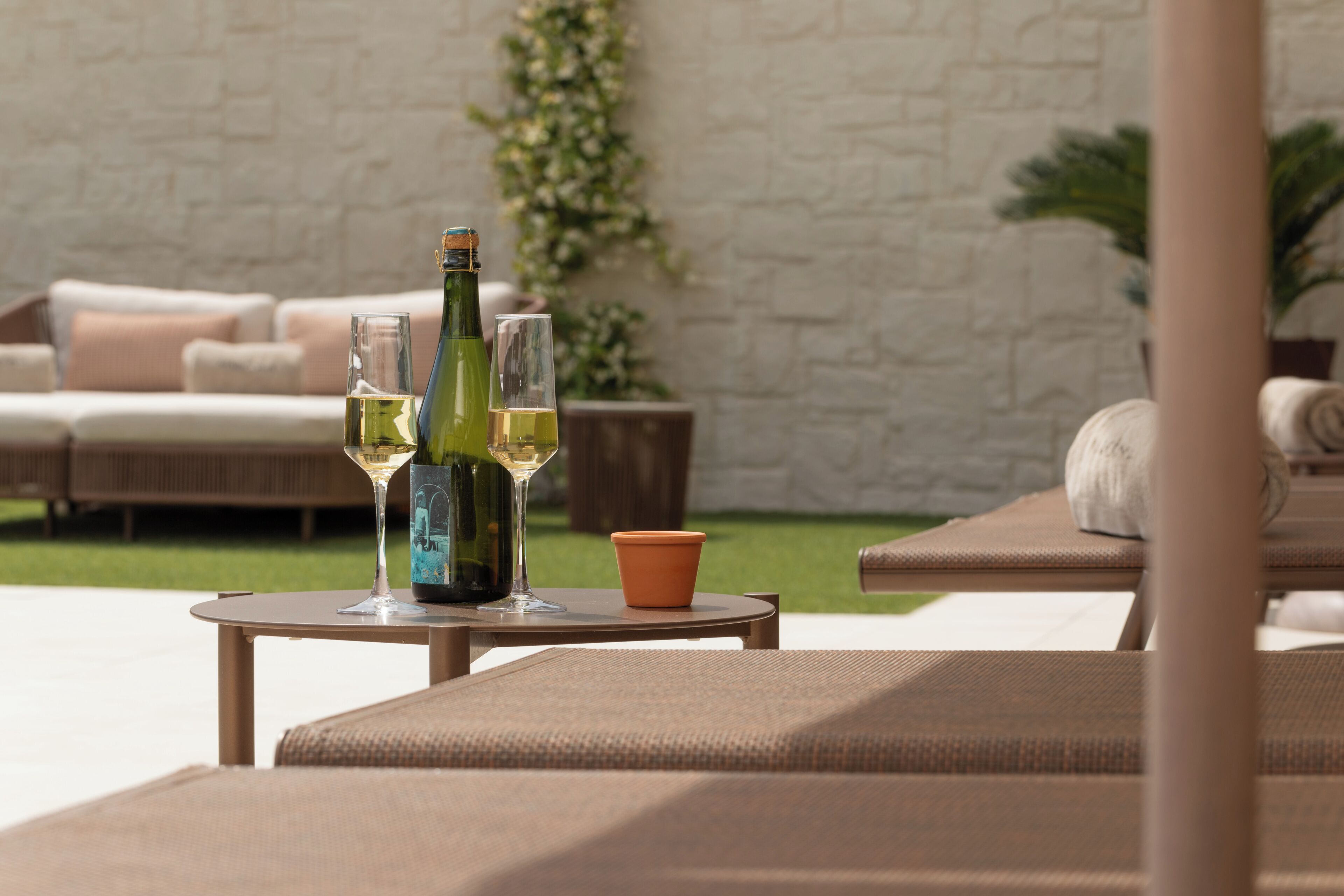 A patio area with a table, two lounge chairs, a bottle of wine, and two glasses.