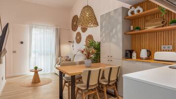 A modern kitchen with wooden cabinets, a dining table with chairs, and a hanging light fixture.