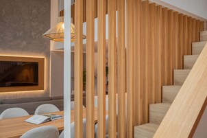 A modern interior with a wooden staircase, a dining area with a table and chairs, and a wall-mounted light fixture.