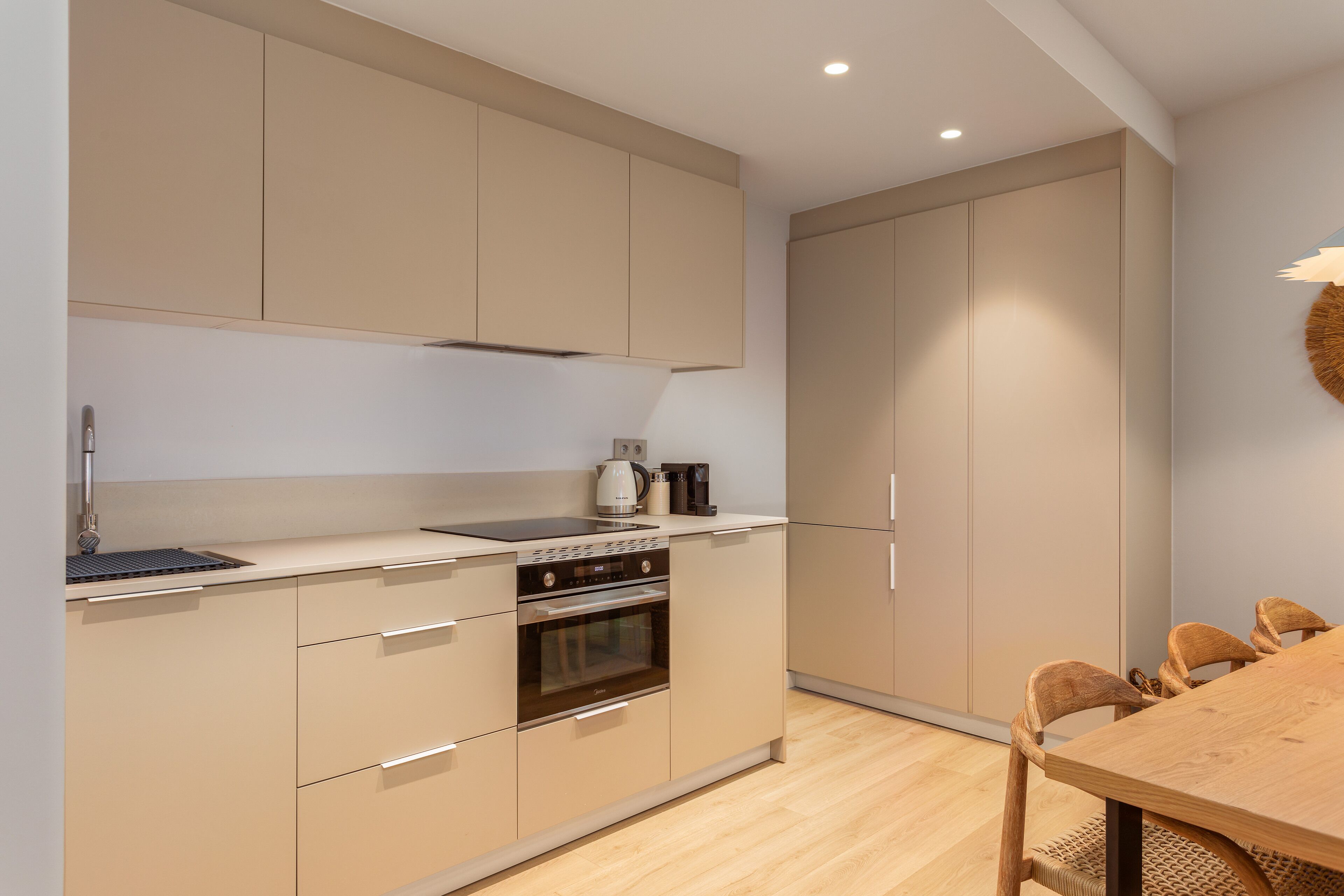 A modern kitchen with beige cabinetry, a built-in oven, and a wooden dining table with chairs.