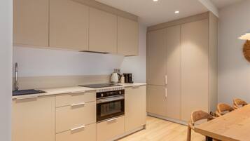 A modern kitchen with beige cabinetry, a built-in oven, and a wooden dining table with chairs.