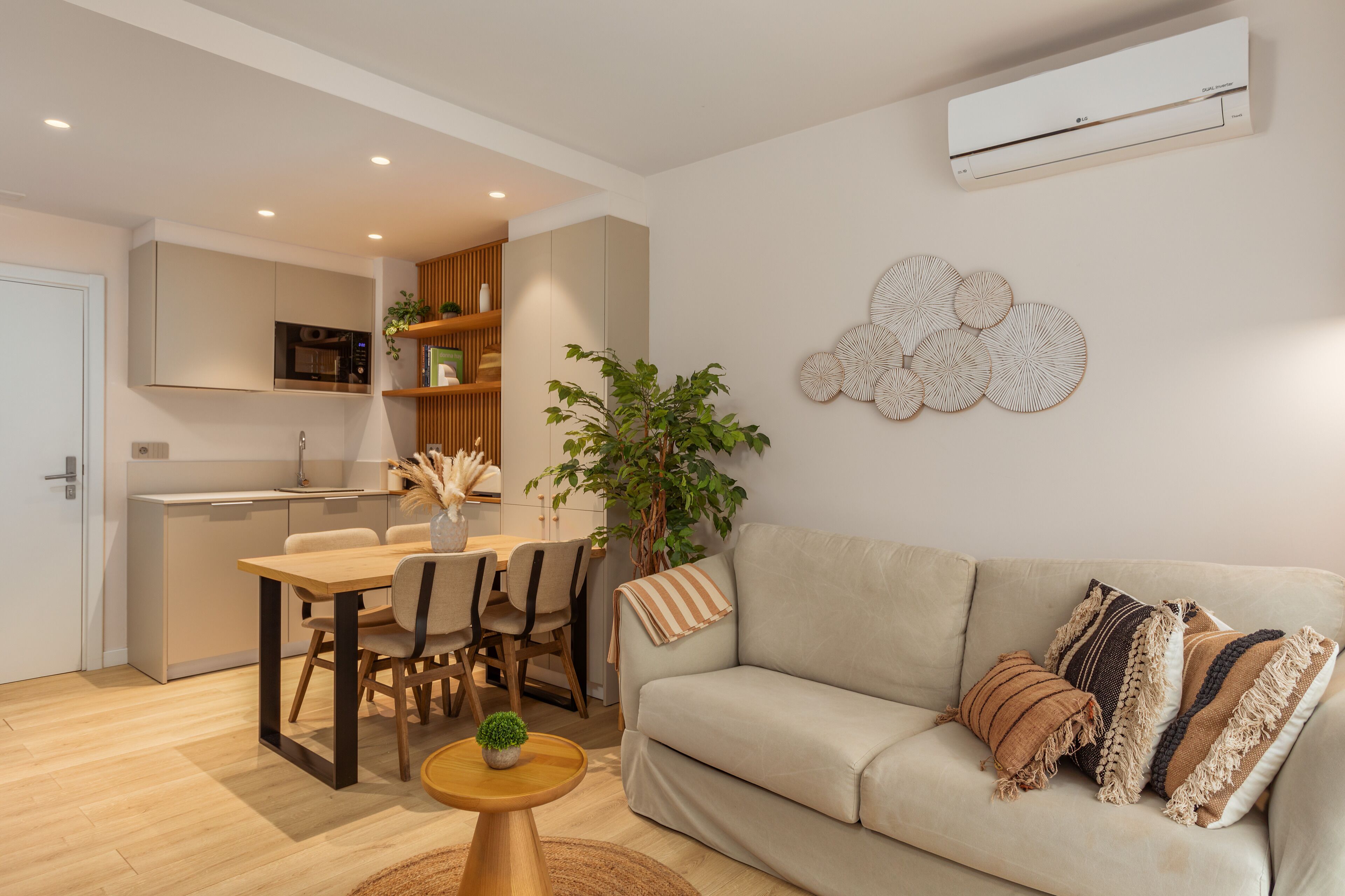 A modern living room with a beige sofa, a dining table, and a kitchen area in the background.
