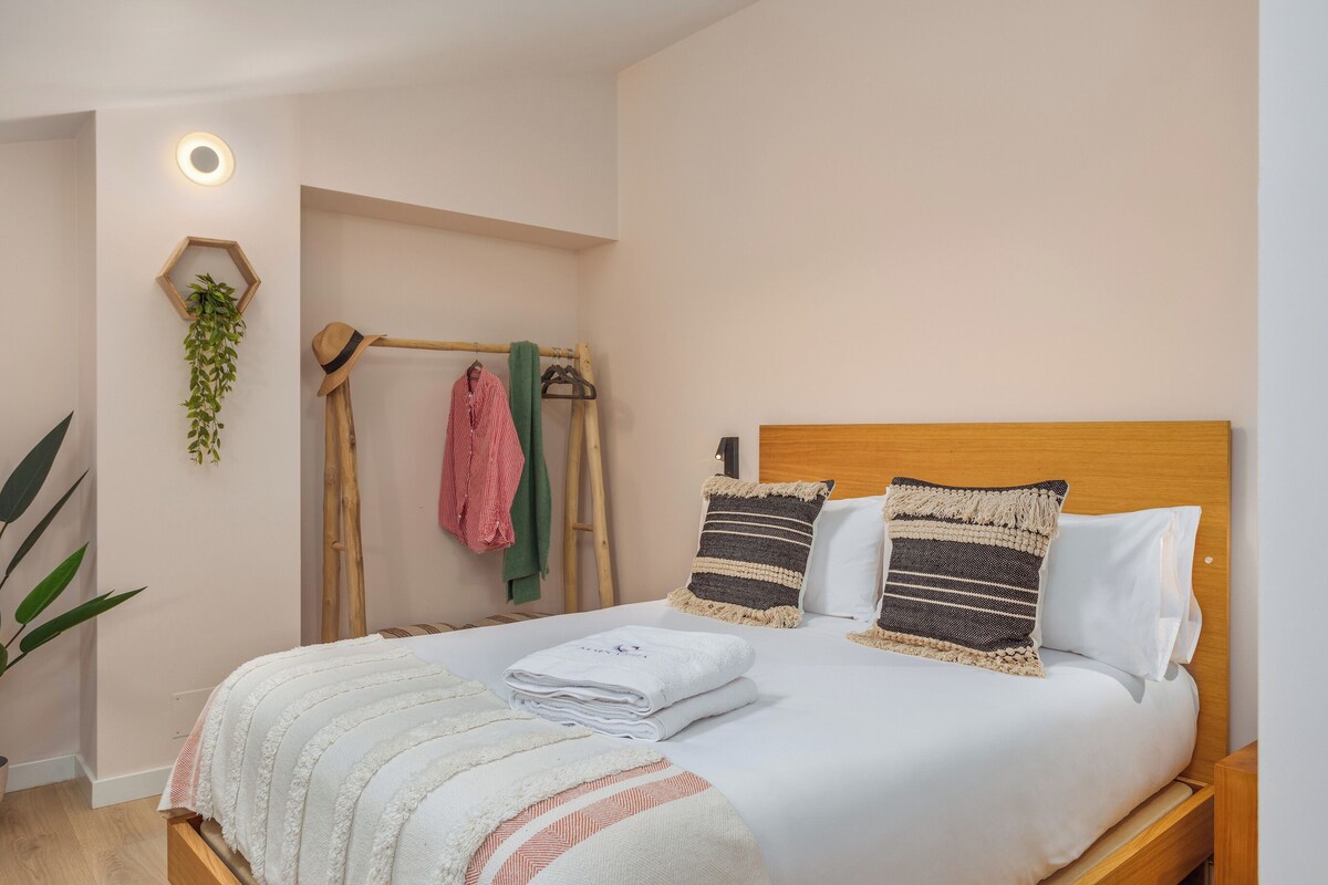 Una cama bien hecha con tablero de madera, dos almohadas y una toalla blanca doblada.
