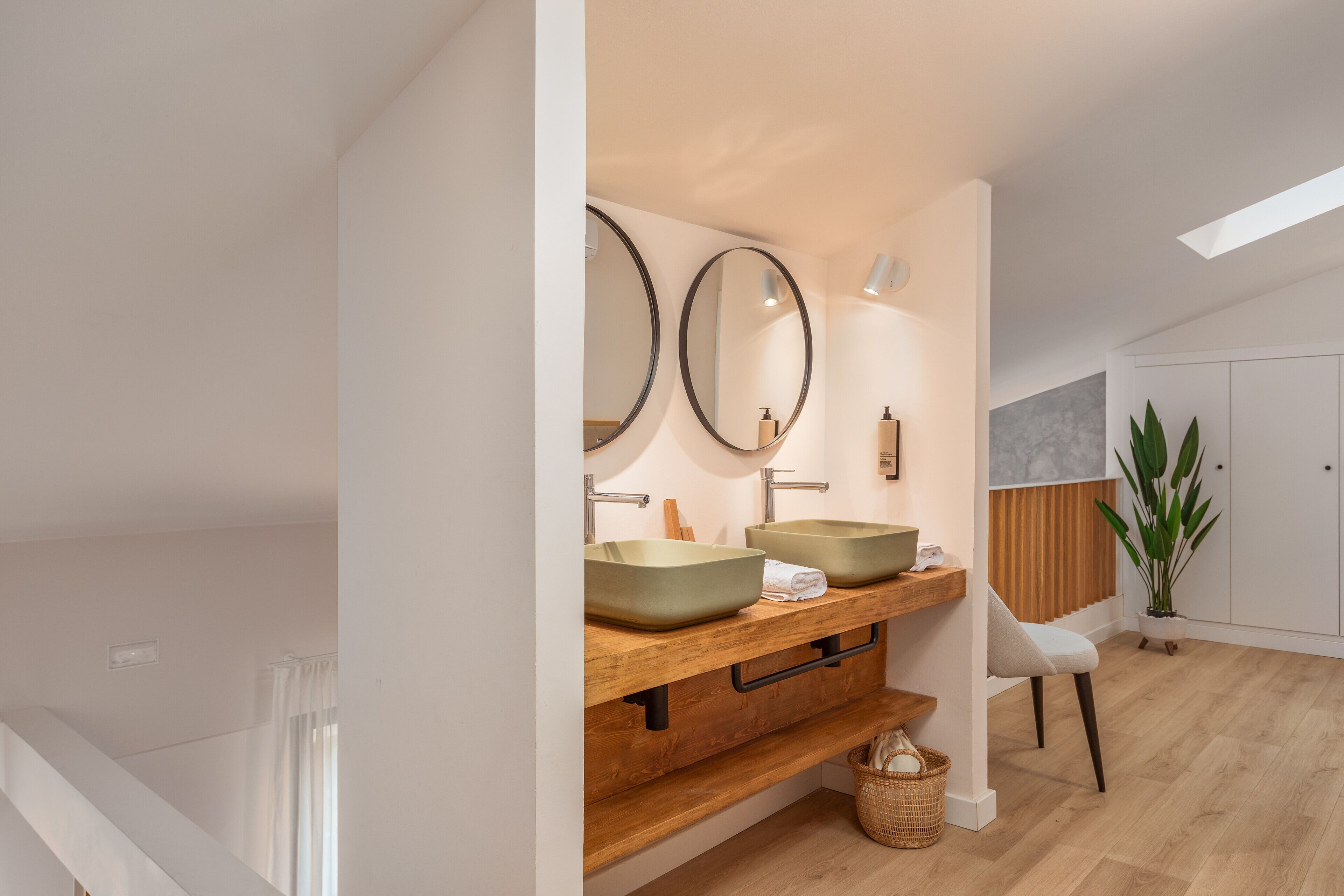 Un baño moderno con dos lavamanos sobre encimera, tocador de madera, espejos grandes y una planta en maceta.