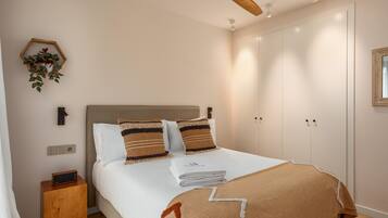 A neatly made bed with a headboard, a bedside table with a radio, a ceiling fan, and a wall-mounted plant.