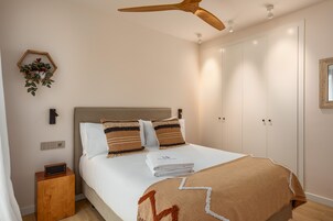 A neatly made bed with a headboard, a bedside table with a radio, a ceiling fan, and a wall-mounted plant.