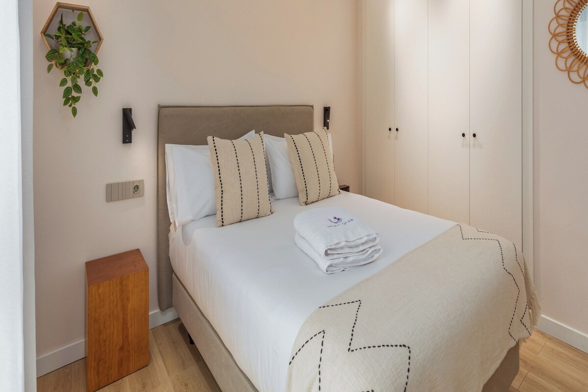 A neatly arranged bedroom with a bed, a ceiling fan, a bedside table, and a wardrobe.
