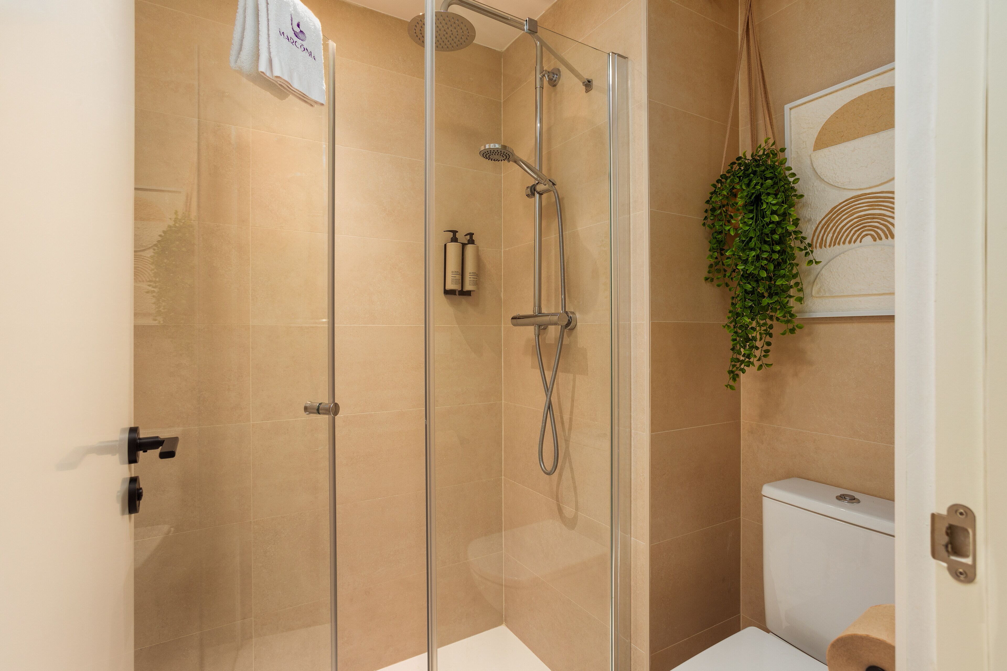 A glass-enclosed shower with a handheld showerhead and a wall-mounted faucet. A towel hangs on the shower door handle.
