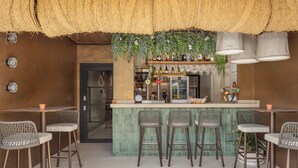 Una zona de bar con mostrador de azulejos verdes, sillas de mimbre y plantas colgantes.