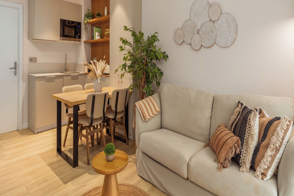 Una sala moderna con un sofá color beige, una mesa de comedor con sillas, una pequeña mesa de centro y una planta en maceta.