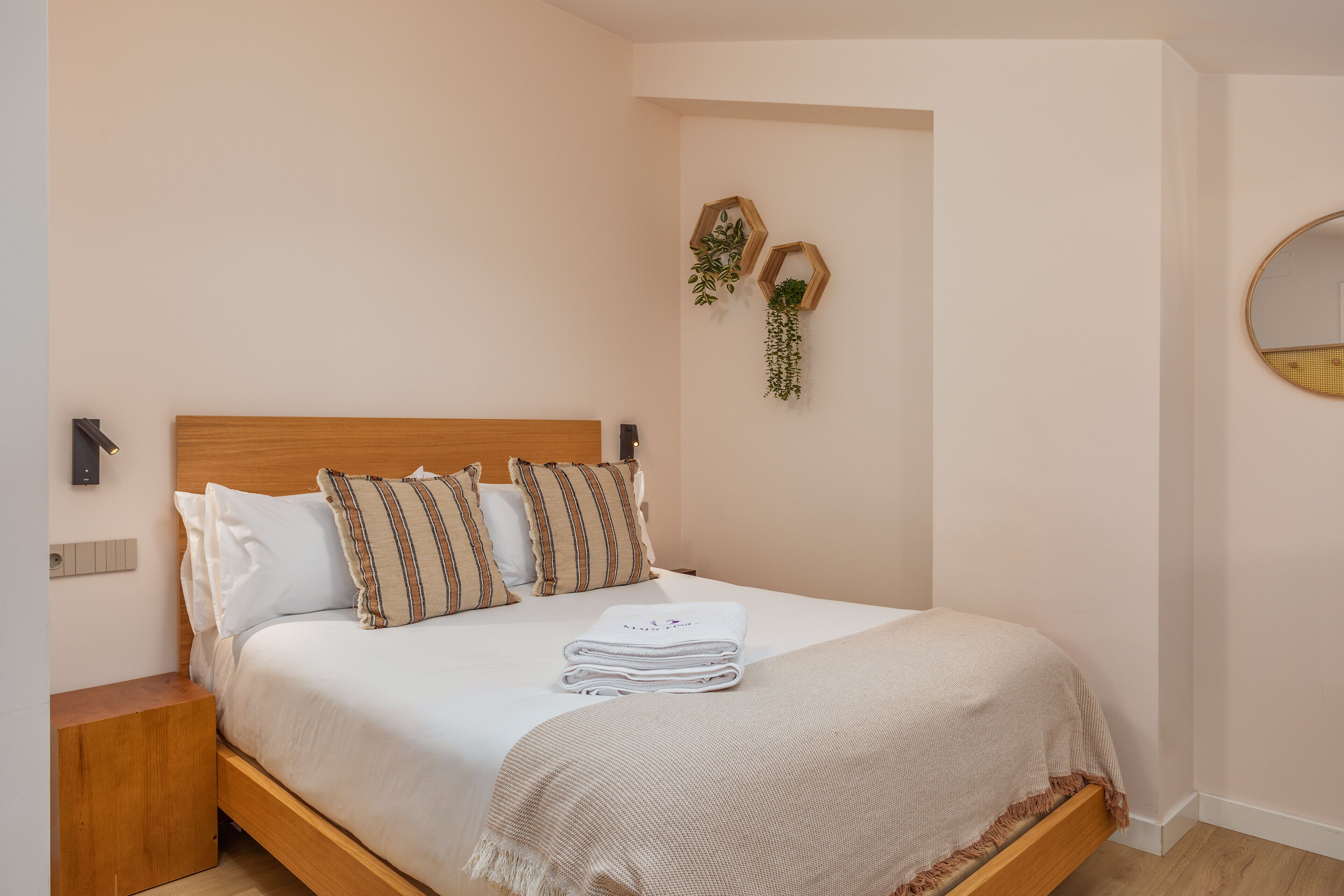 Een keurig opgemaakt bed met een houten hoofdbord, een nachtkastje en twee zeshoekige decoraties aan de muur met planten.
