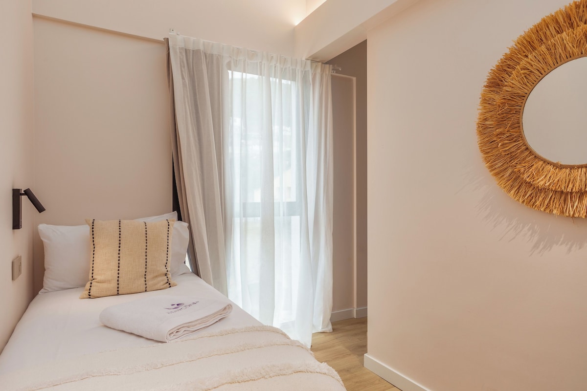 A bedroom with a bed, a wall-mounted mirror, and sheer curtains.