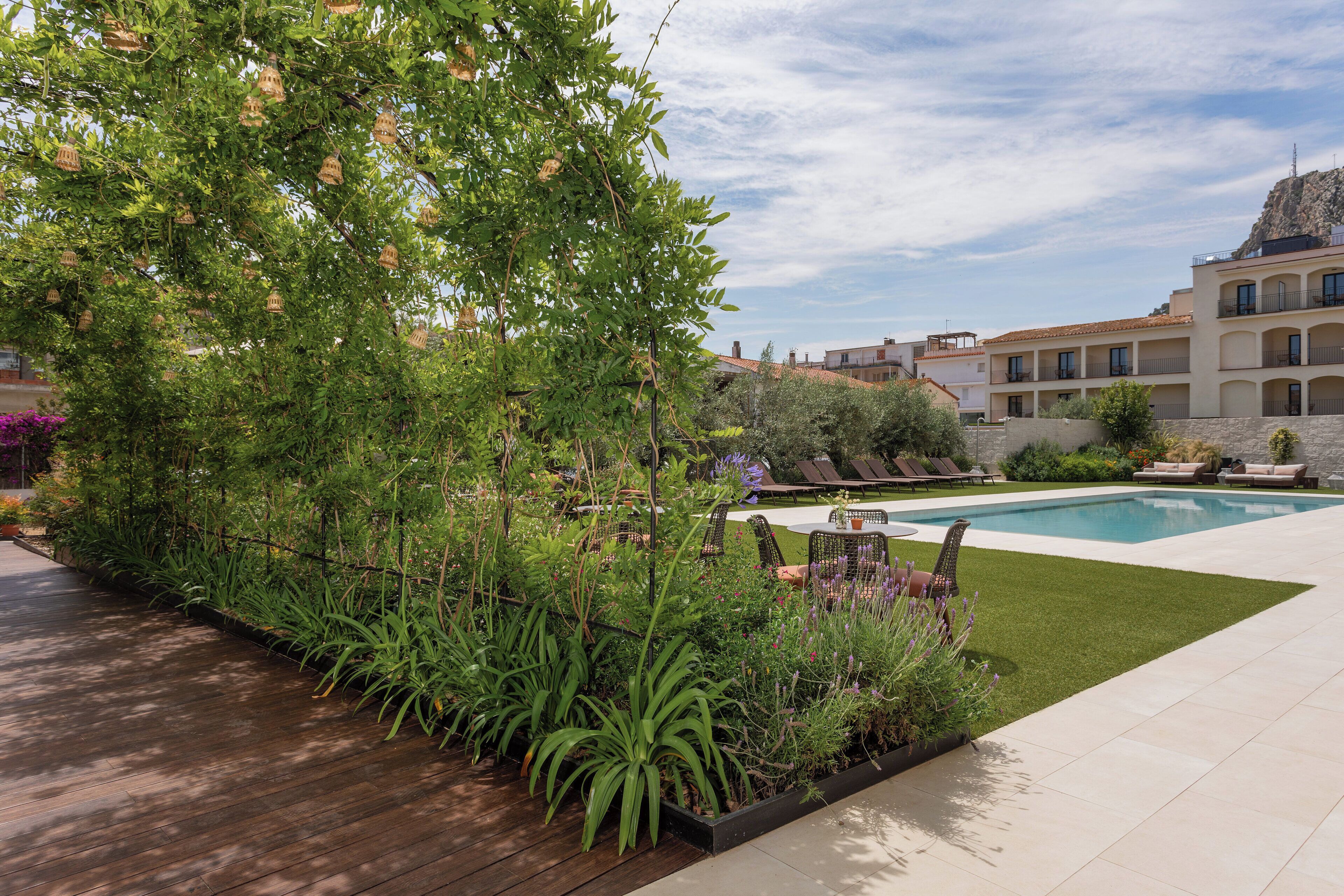 A landscaped outdoor area with a pool, wooden deck, and a building with balconies in the background.