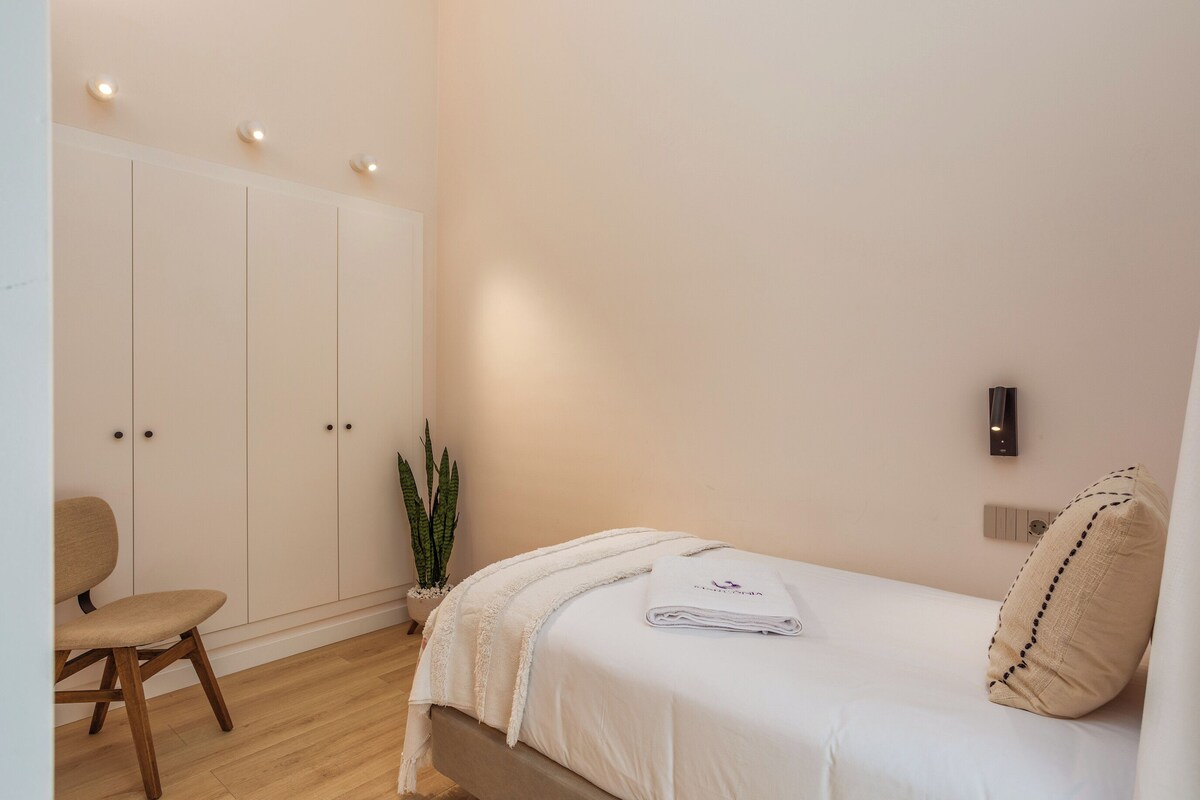 A bedroom with a bed, a chair, a wardrobe, and a wall-mounted light.