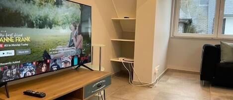 A living room with a flat-screen TV on a wooden stand, a remote control, and a cable management system.