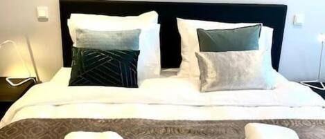 Una cama bien hecha con una colcha estampada, dos almohadas y dos toallas dobladas sobre la cama.