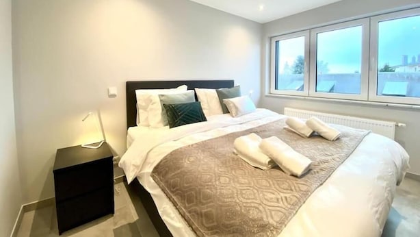 A modern bedroom with a large bed, a nightstand, and a window with a city view. - 2 bedrooms in the heart of Limpertsberg (Luxembourg City)