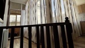 A spacious room with a wooden floor, a large window with patterned curtains, and a kitchen area visible through the window. - Opera Apartment Sleeps 4 With Patio (Tbilisi)