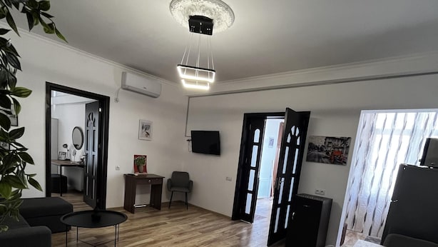 A spacious living area with a wooden floor, a dining table, and a TV mounted on the wall. - Opera Apartment Sleeps 4 With Patio (Tbilisi)