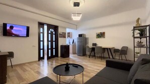 A modern living room with a flat-screen TV, a dining area with chairs, a kitchen, and a grey sofa. - Opera Apartment Sleeps 4 With Patio (Tbilisi)