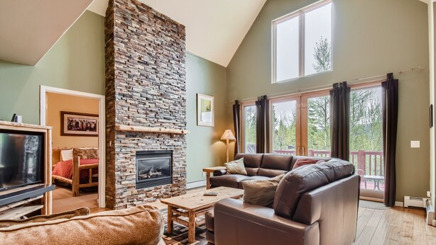 A cozy living room with a stone fireplace, a leather sofa, a coffee table, and a TV. - Expansive townhome, Private hot tub, Great Location, 42BC (Silvethorne)