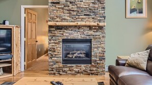 A living room with a stone fireplace, wooden entertainment unit, and a leather sofa. - Expansive townhome, Private hot tub, Great Location, 42BC (Silvethorne)