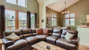 A spacious living room with a large L-shaped leather sofa, a wooden coffee table, and a view of the outside balcony. - Expansive townhome, Private hot tub, Great Location, 42BC (Silvethorne)
