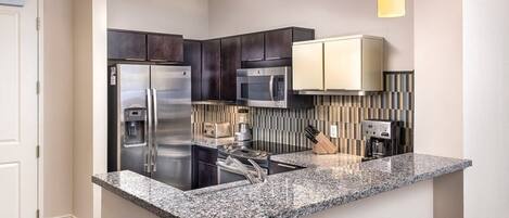 A modern kitchen with dark cabinets, stainless steel appliances, a granite countertop, and two woven stools.