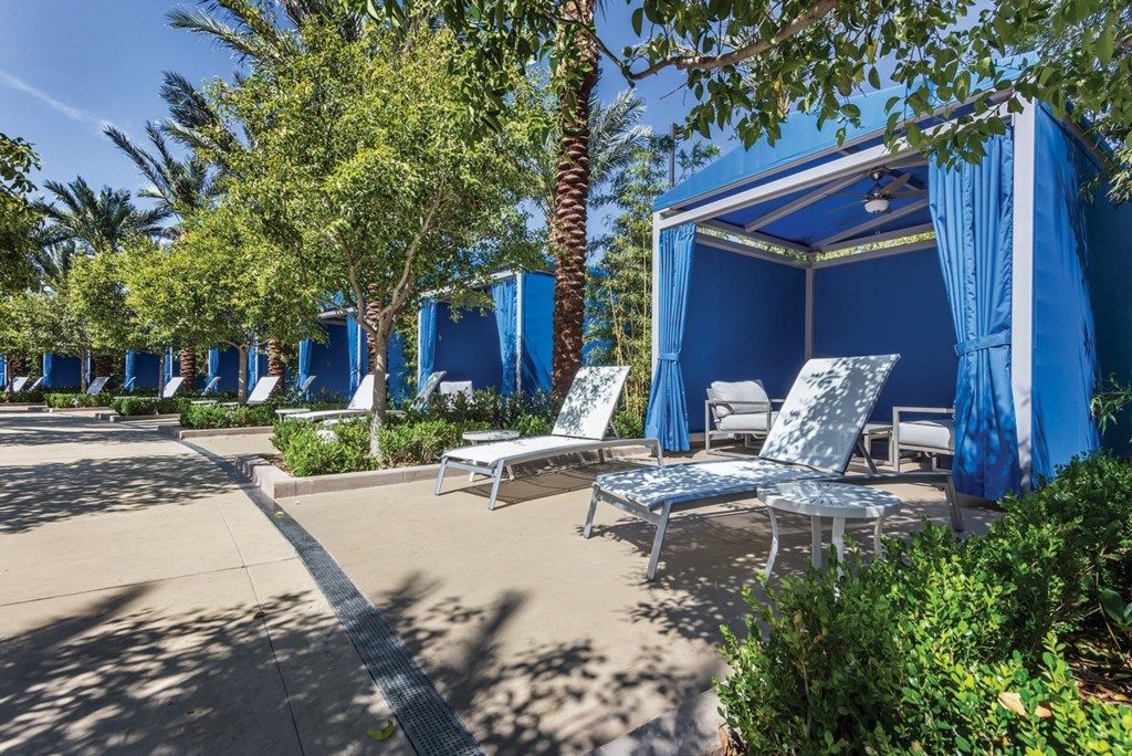 A row of outdoor lounge areas with blue canopies, white lounge chairs, and palm trees.