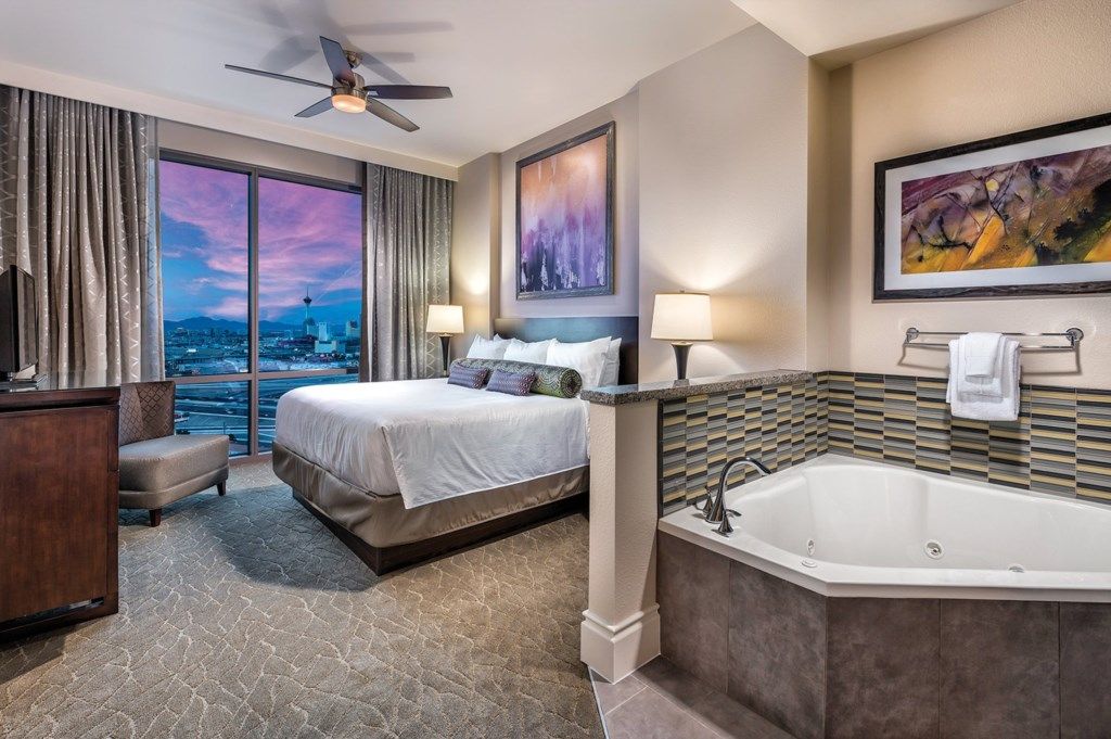 Une chambre d’hôtel avec un grand lit, une baignoire, un bureau et une vue sur le paysage urbain.
