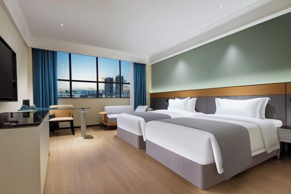 A hotel room with a city view, two beds, a desk, and a chair.