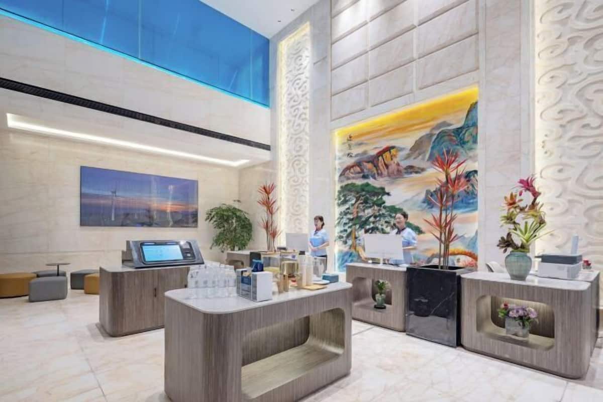 A modern reception area with a high ceiling, a large mural, and reception desks with plants.