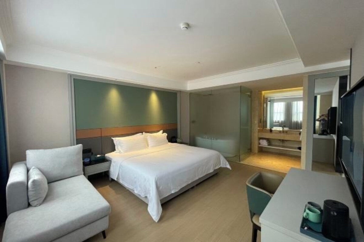 A modern hotel room with a bed, a sofa, a desk, and a TV.