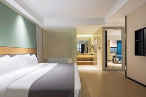 Habitación de hotel con una cama grande, un vestidor, un baño con espejo y un televisor en la pared.