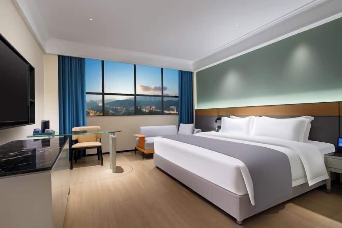 A modern hotel room with a large bed, a desk with a glass top, a chair, and a TV.