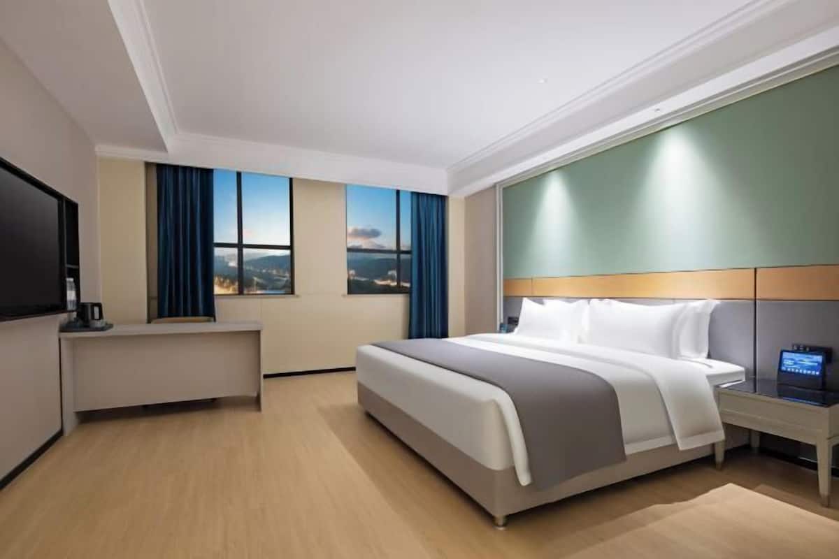A hotel room with a bed, a desk, a TV, and a view of the cityscape.