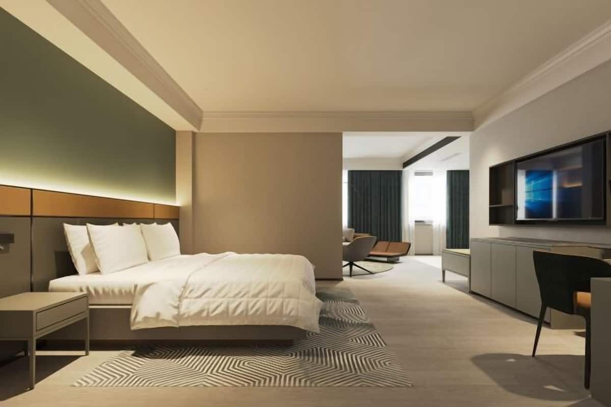 A modern hotel room with a bed, a desk, a chair, a TV, and a view of the city.
