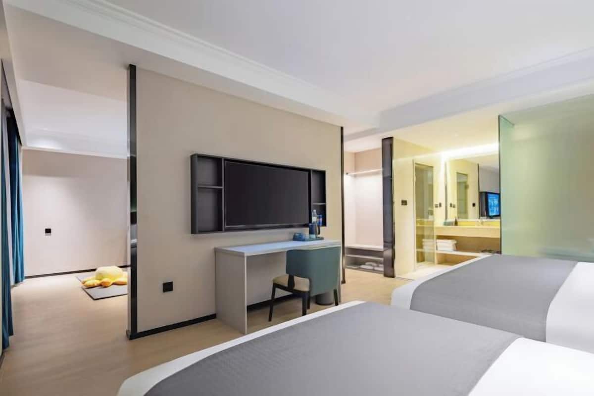 A hotel room with a bed, a desk, a chair, a television, and a bathroom visible through an open door.