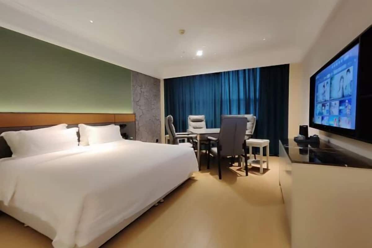 A hotel room with a bed, a desk, a chair, a TV, and a large window.