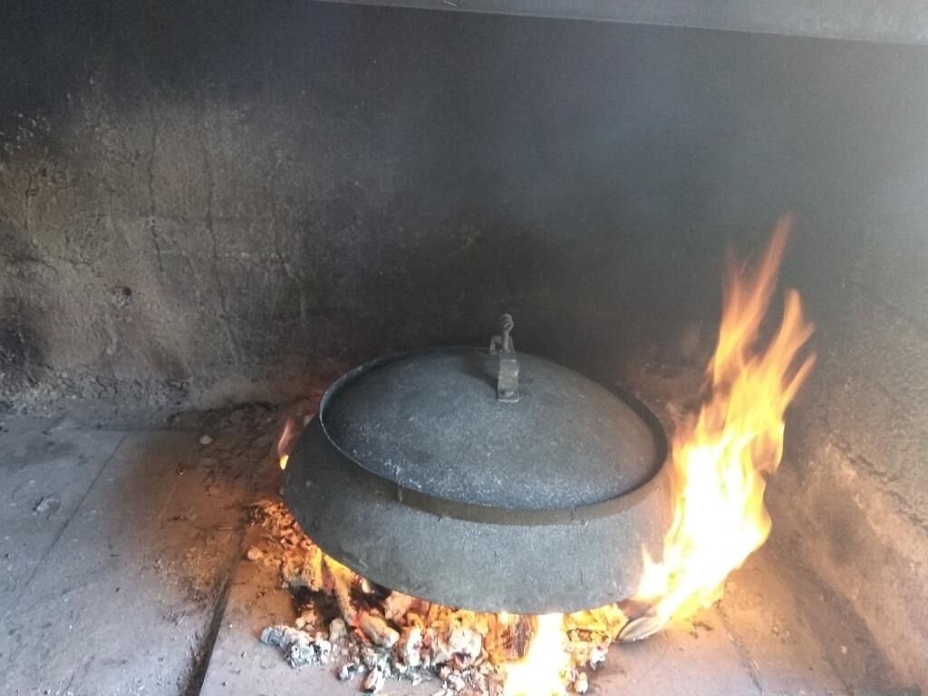 A traditional stove with a pot on top, flames underneath, and a metal lid.