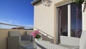 A balcony with wicker furniture, a glass table, and a potted plant.
