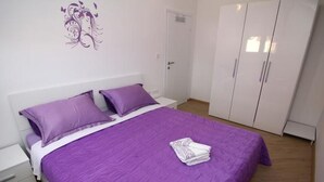 A bedroom with a large bed, purple bedding, a white wardrobe, and a decorative wall piece.