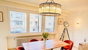 Ein Essbereich mit einem Holztisch, sechs roten Stühlen, einer Blumenvase, einem Heizkörper und einem Fenster mit Blick auf Gebäude.