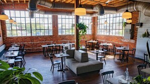 Een restaurant met bakstenen muren, houten vloeren en grote ramen. Tafels en stoelen staan klaar voor diners.