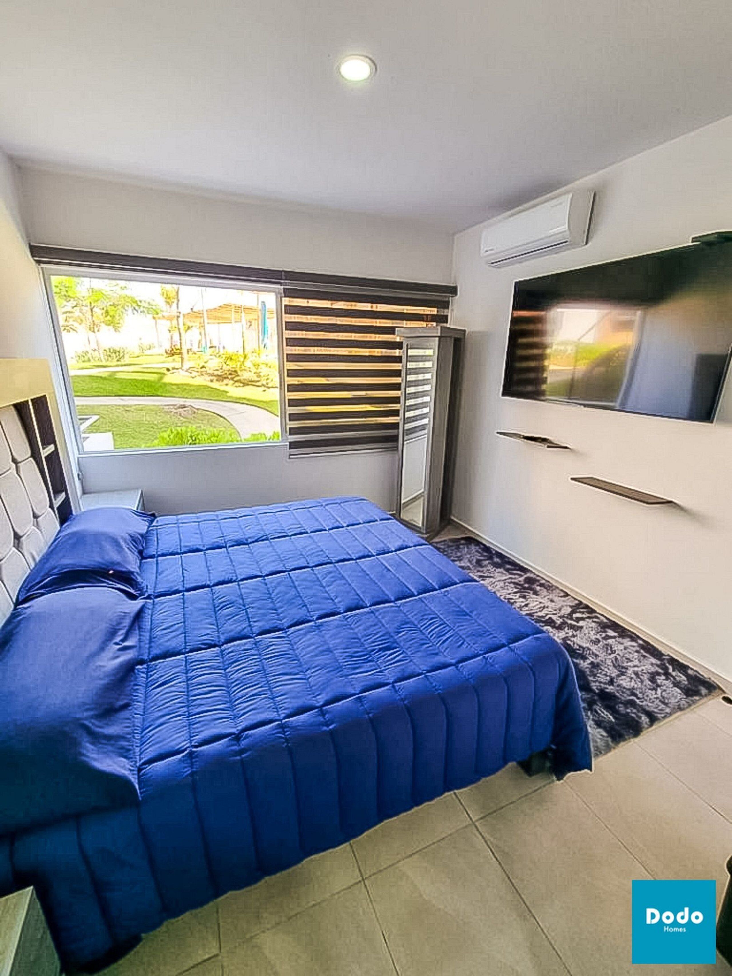 Un dormitorio con cama, televisor, ventana con persianas y un pequeño balcón.