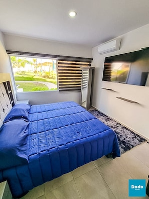 Une chambre à coucher avec un lit, une télévision, une fenêtre avec des stores et un petit balcon.