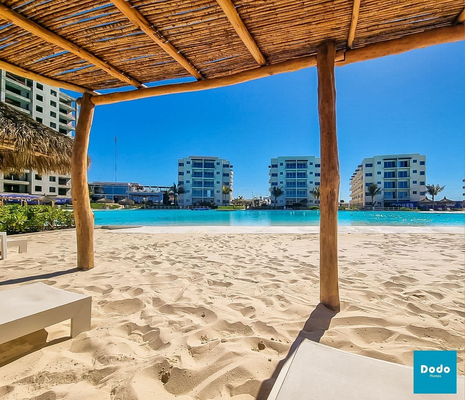 Ein Strand mit einer Holzkonstruktion, blauem Himmel und mehreren mehrstöckigen Gebäuden im Hintergrund.