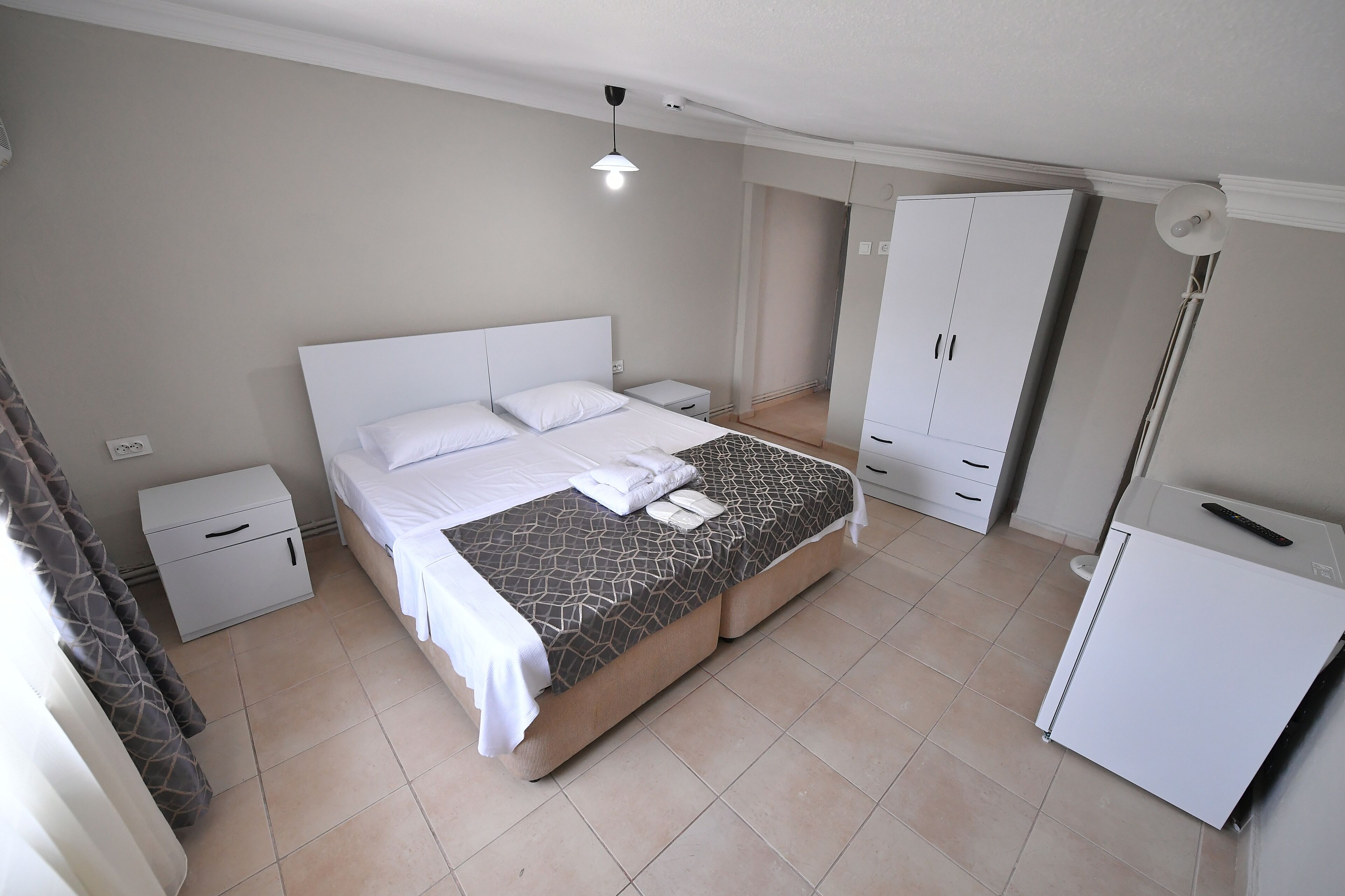 A bedroom with a bed, nightstands, a wardrobe, and a refrigerator.
