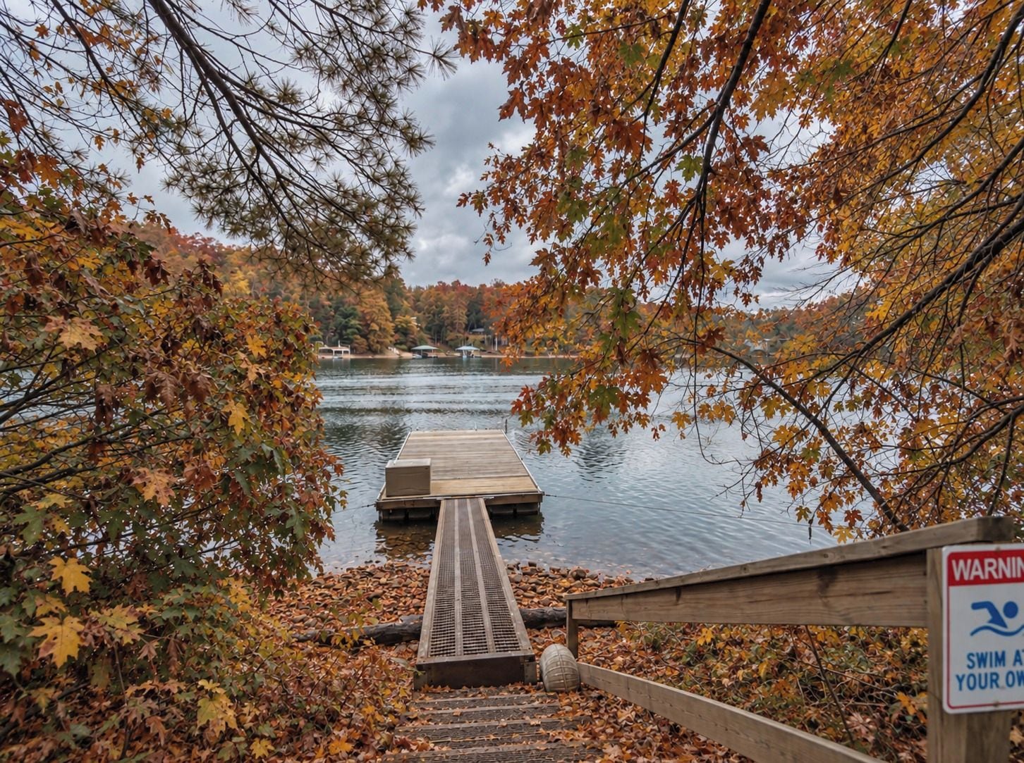 A wooden dock leading to a calm lake surrounded by autumn foliage.